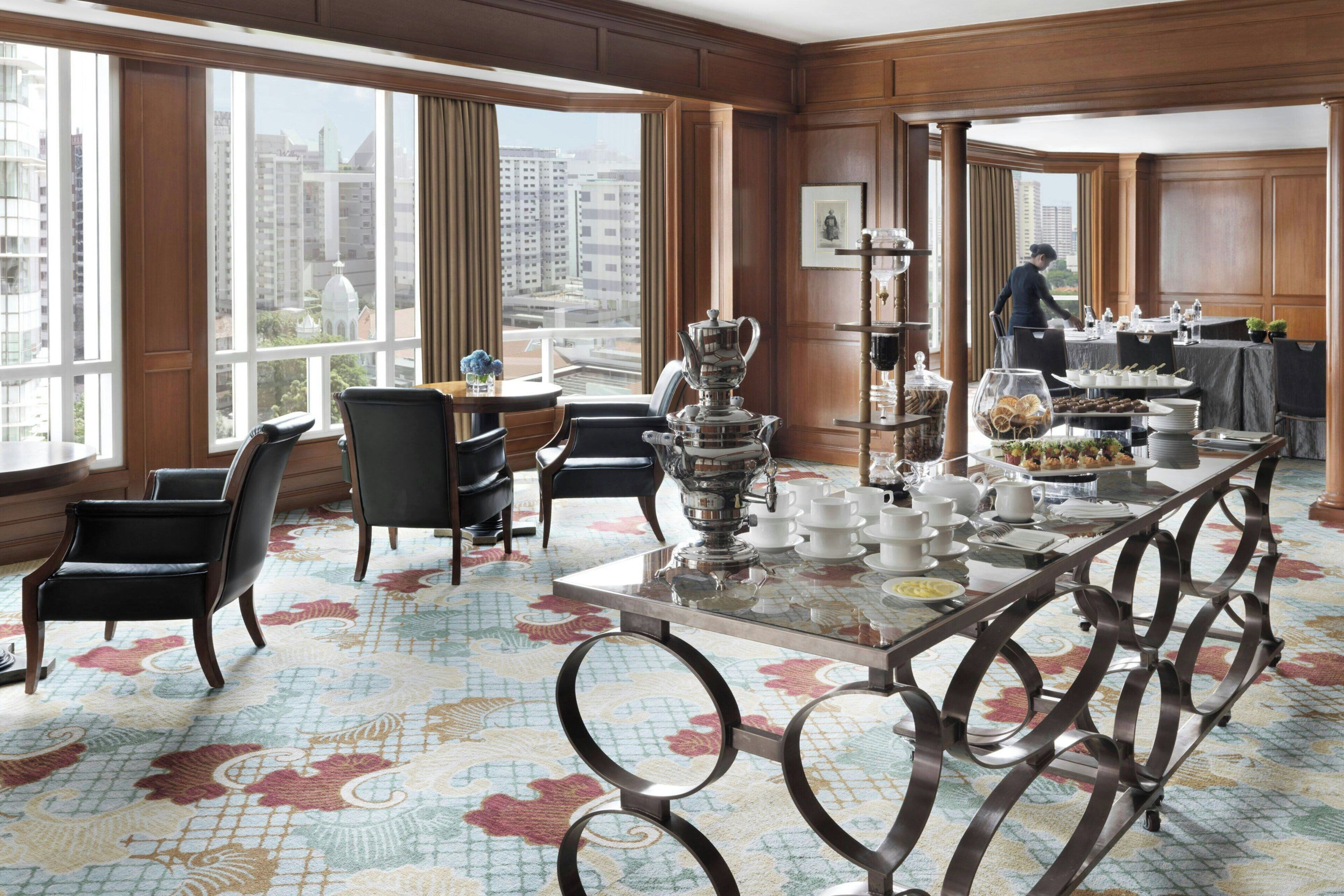 Un comedor de hotel con una mesa grande dispuesta para el desayuno, sillas y vistas de la ciudad a través de amplios ventanales.