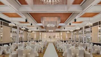 A banquet hall with a central aisle, chandeliers, and white decor.