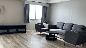 A modern living room with a grey sofa, two armchairs, a coffee table, and a large window with curtains. - Days Inn by Wyndham Sioux Falls Airport (Sioux Falls)