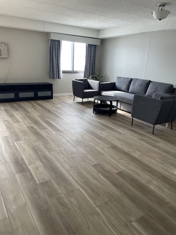 A modern living room with a grey sofa, two armchairs, a coffee table, and a large window with curtains. - Days Inn by Wyndham Sioux Falls Airport (Sioux Falls)