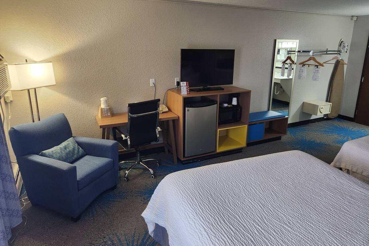Habitación de hotel con escritorio, silla, televisor, minibar y dos camas.
