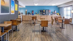 A modern cafe with wooden tables and chairs, a blue accent wall, and a counter with various items. - Days Inn by Wyndham Sioux Falls Airport (Sioux Falls)