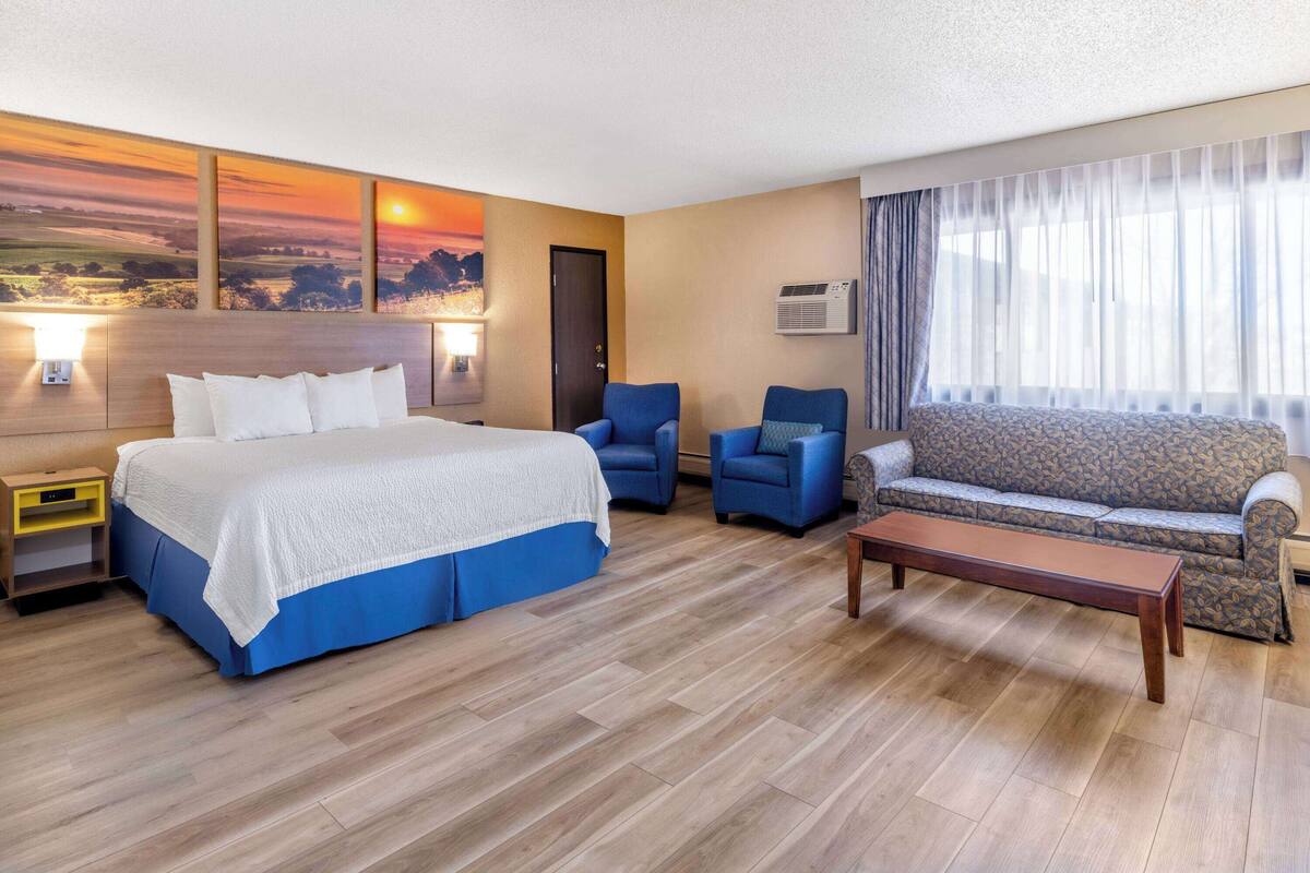 Un cuarto de hotel con cama, dos sillones, un sofá, una mesita de madera y un cuadro en la pared.