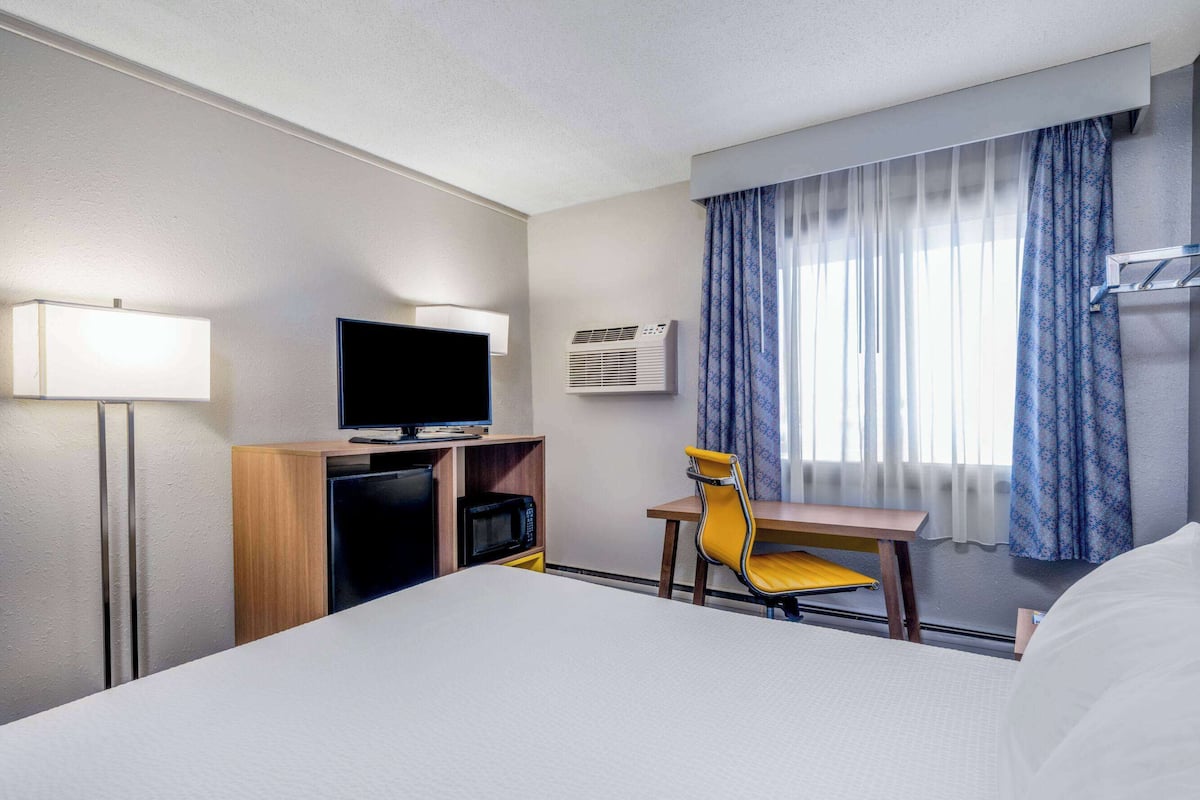 Habitación de hotel con cama, escritorio, silla, televisor, refrigerador y aire acondicionado.
