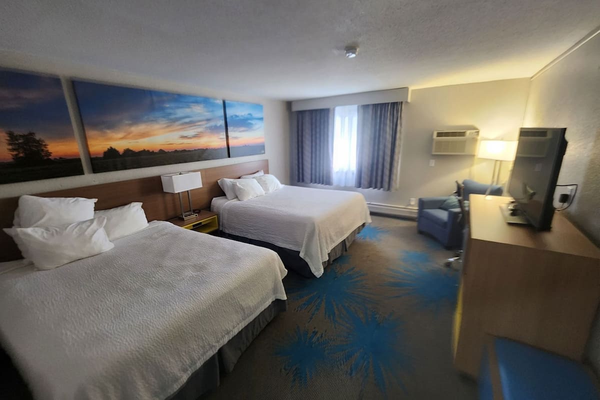 Una habitación de hotel con dos camas, un escritorio con televisor, una ventana con cortinas y un cuadro en la pared.