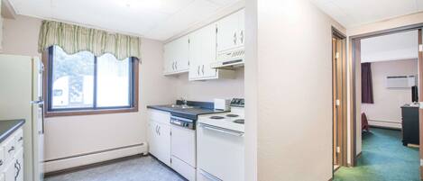 A compact kitchen with white cabinets, a stove, and a window with a green valance.