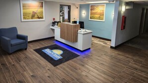 A reception area with a wooden reception desk, a blue chair, and two framed landscape paintings on the walls. - Days Inn by Wyndham Sioux Falls Airport (Sioux Falls)