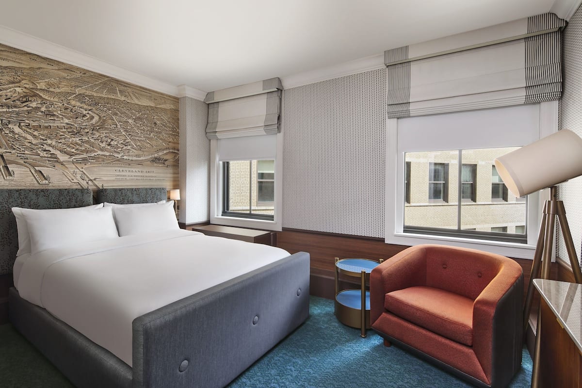 A hotel room with a large bed, a small table, a chair, and a map on the wall.
