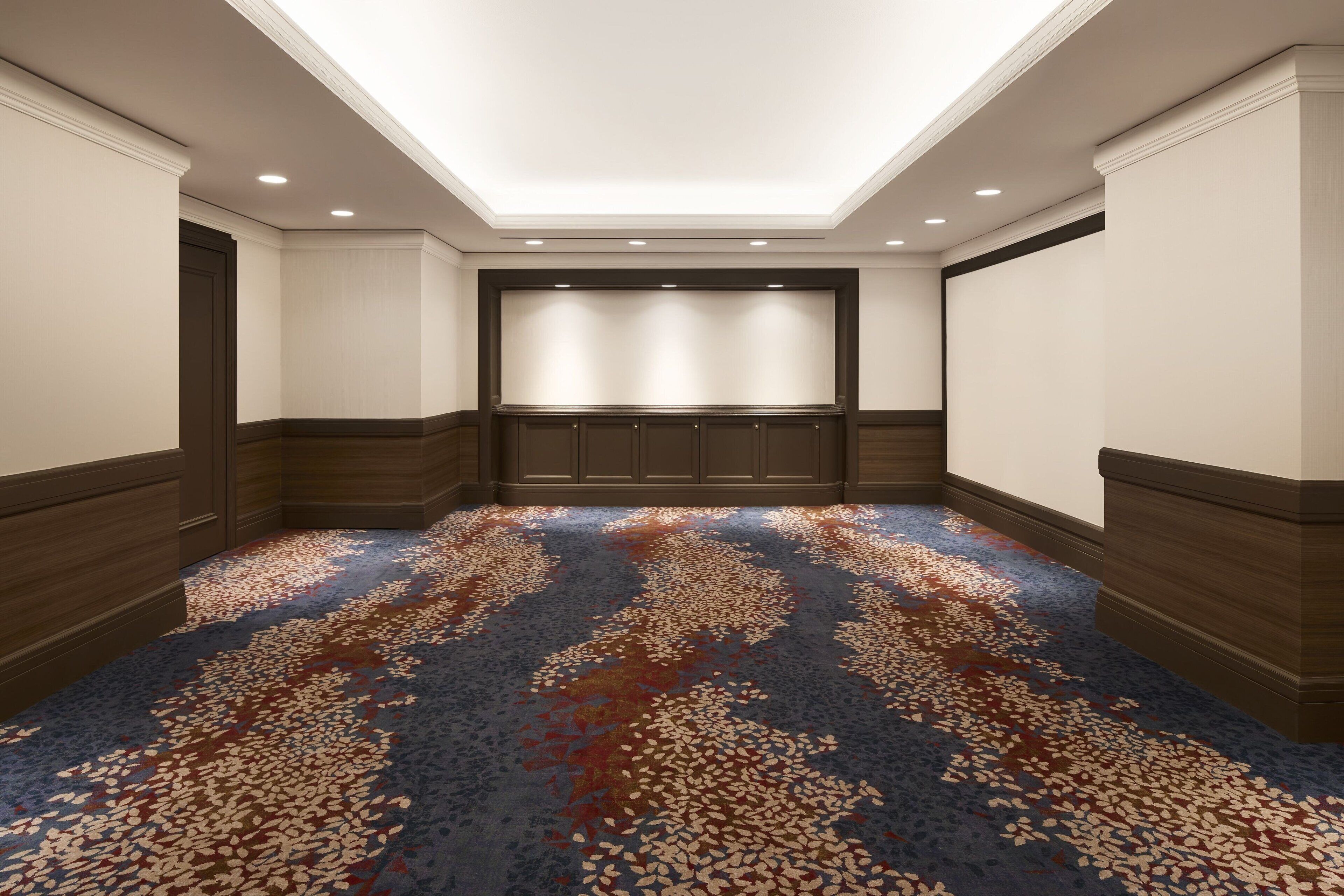 A hotel hallway with a patterned carpet, wooden paneling, and recessed ceiling lighting.