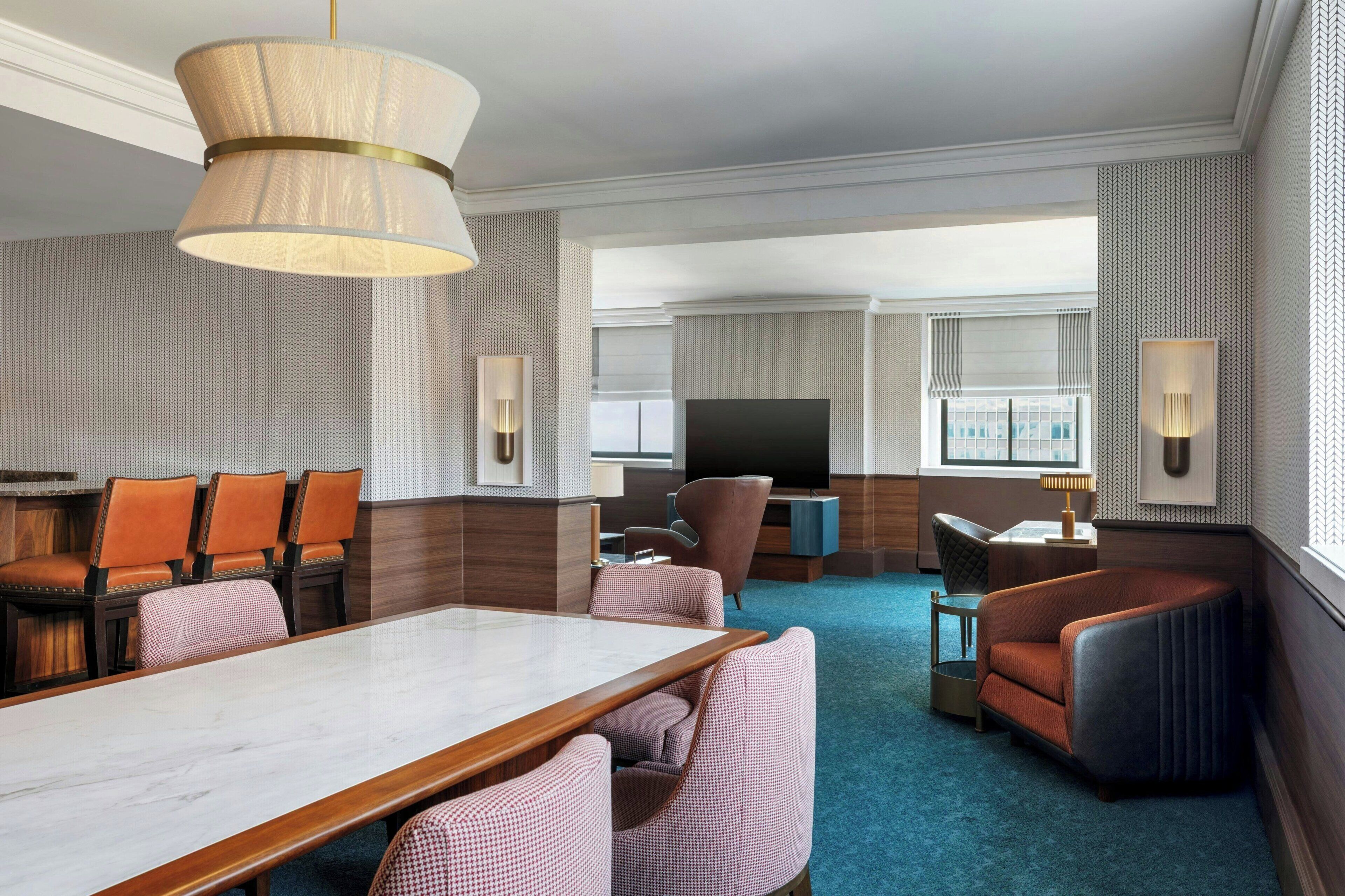 A hotel room with a dining area, a living area with a TV, and a large window.