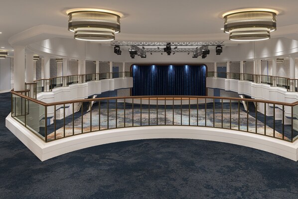 A grand hotel lobby with a curved staircase, a blue curtain backdrop, and modern chandeliers.