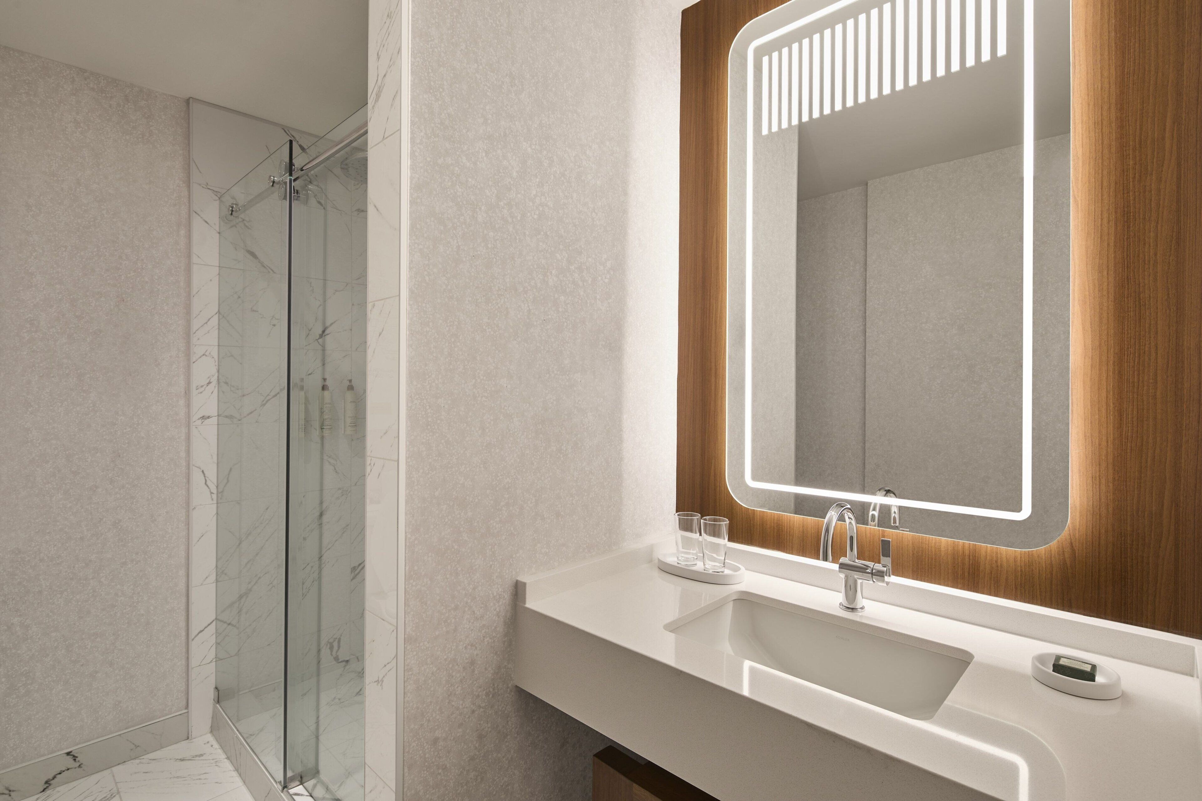 A modern bathroom with a glass shower, a white sink, and a mirror with a wooden frame.