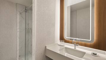 A modern bathroom with a glass shower, a white sink, and a mirror with a wooden frame.