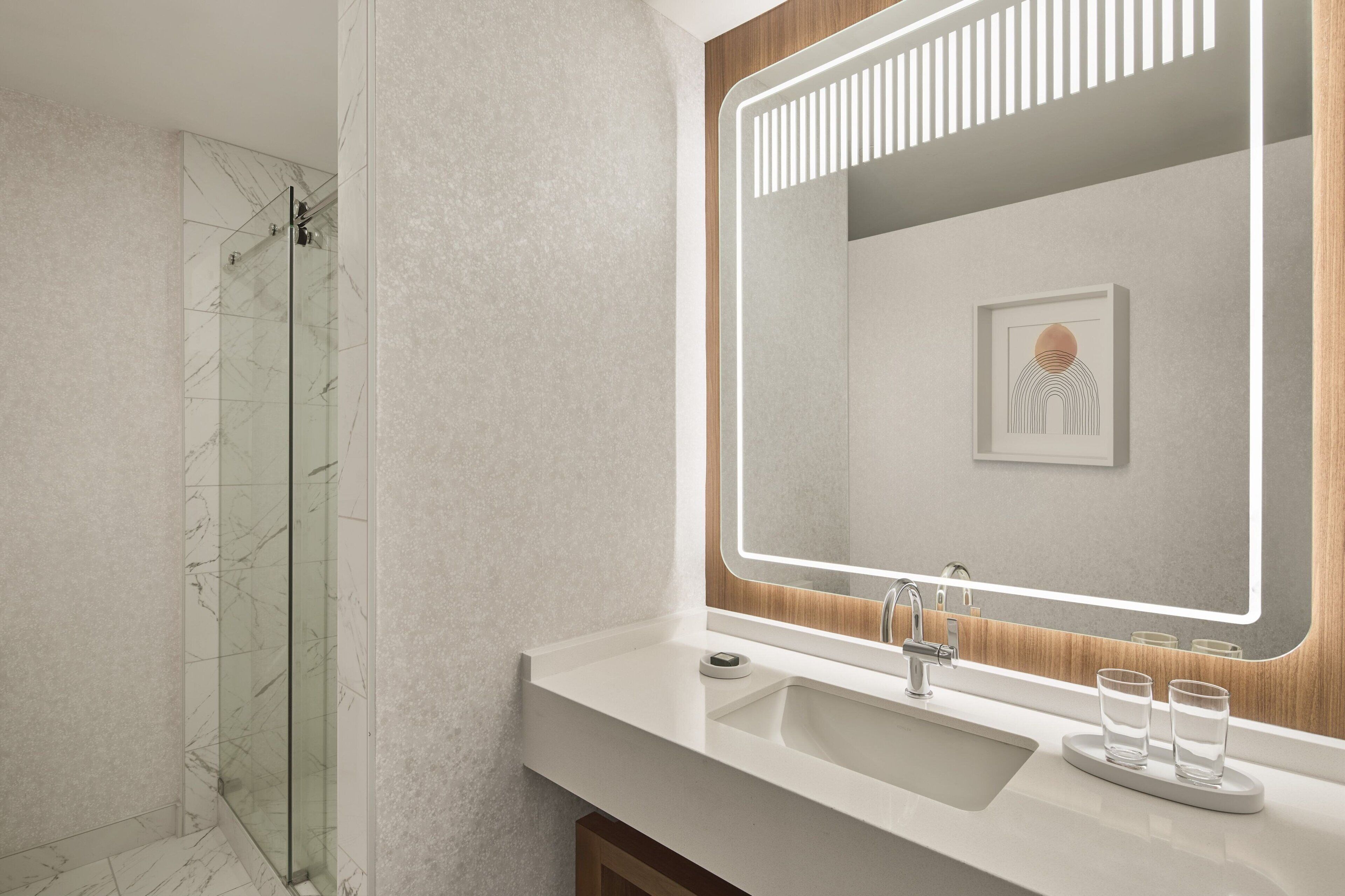 Un baño moderno con cabina de ducha de vidrio, un espejo grande y un lavamanos blanco.