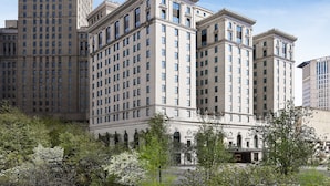 A large, historic building with multiple floors and a symmetrical facade, surrounded by trees and other buildings.