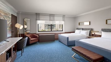 A hotel room with a bed, a desk, a chair, a bench, a TV, and a window with a view of buildings.
