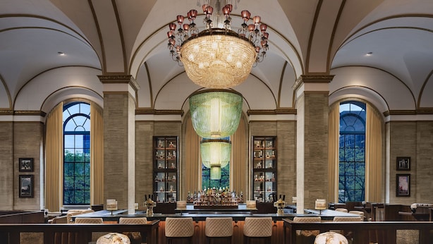 A bar area with a large chandelier, bar stools, and a long counter.
