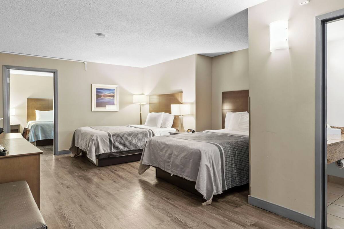 A hotel room with two beds, a desk, and a mirror.