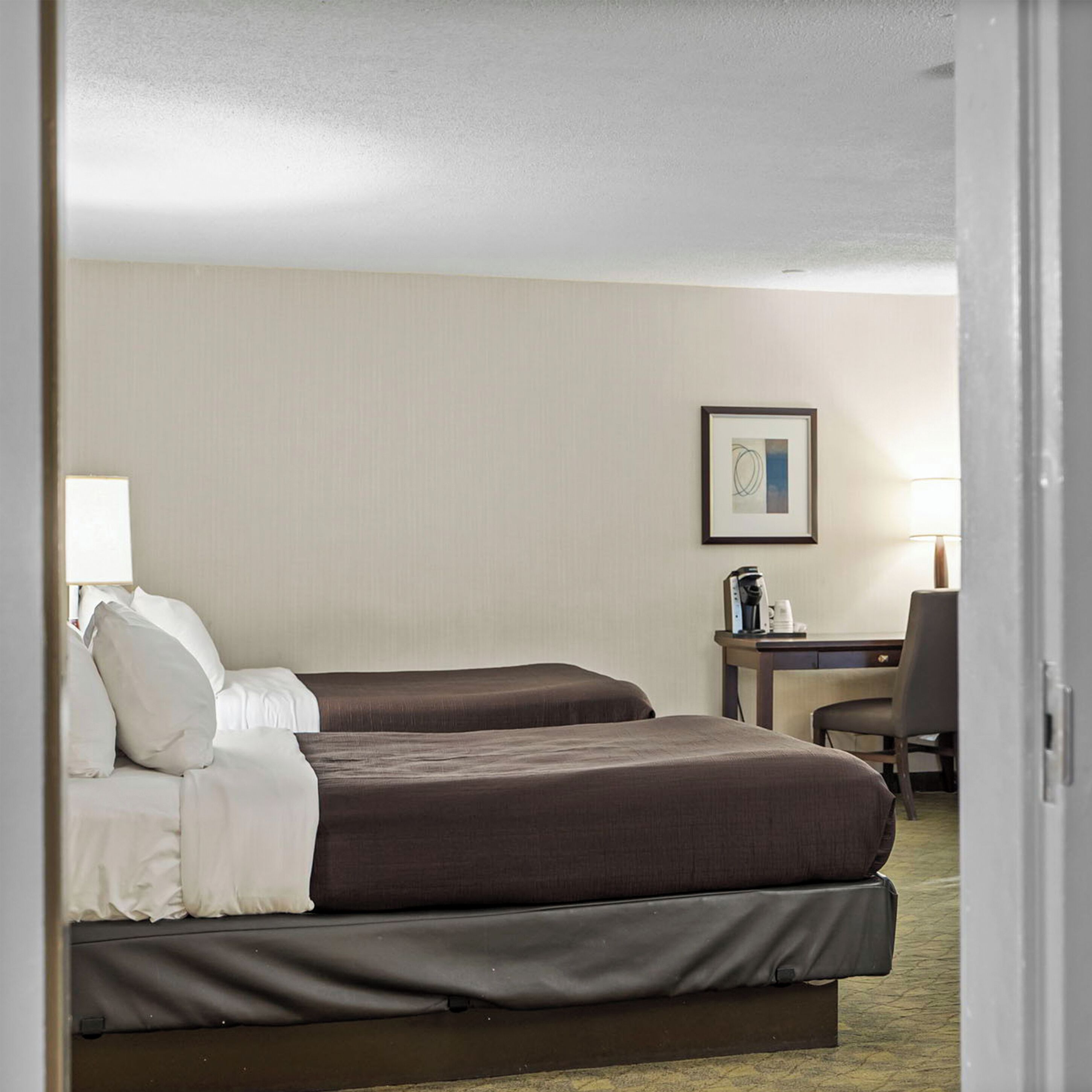 A hotel room with two beds, a desk, a chair, and a framed picture on the wall.
