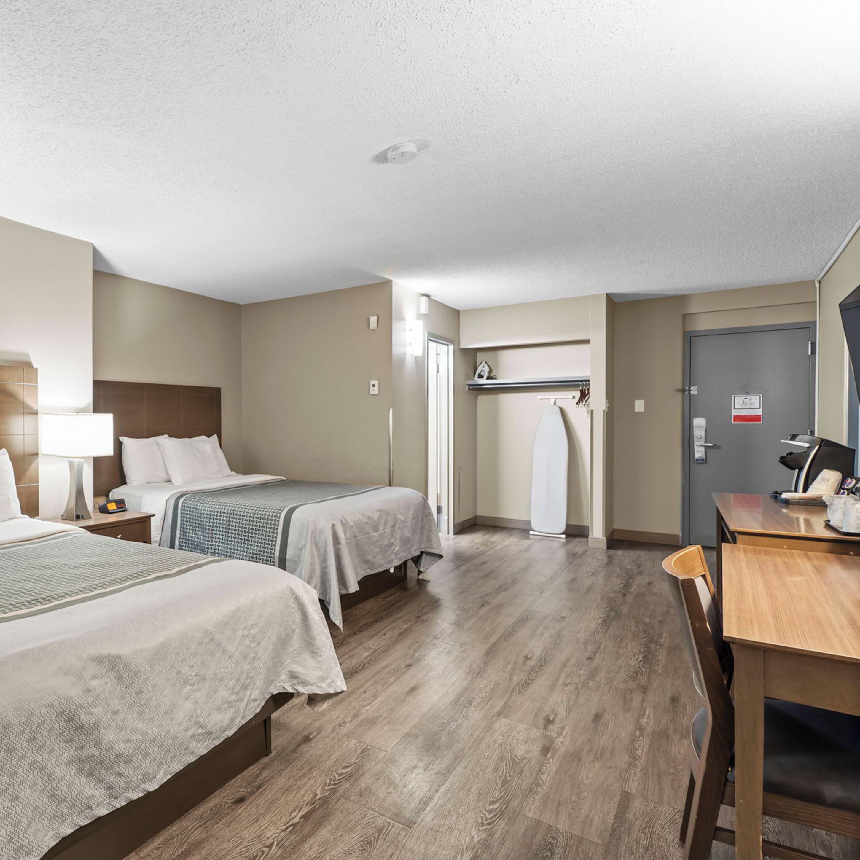 A hotel room with two beds, a desk, a chair, a wardrobe, and a door.