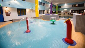 Una piscina interior con múltiples fuentes y un edificio de varios niveles al fondo.