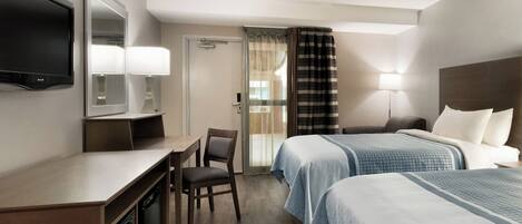 A hotel room with two beds, a desk with a chair, a television, and a bathroom door.