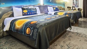 Habitación de hotel con cubrecama con motivos espaciales, un mural de un astronauta y planetas, y una lámpara de techo.