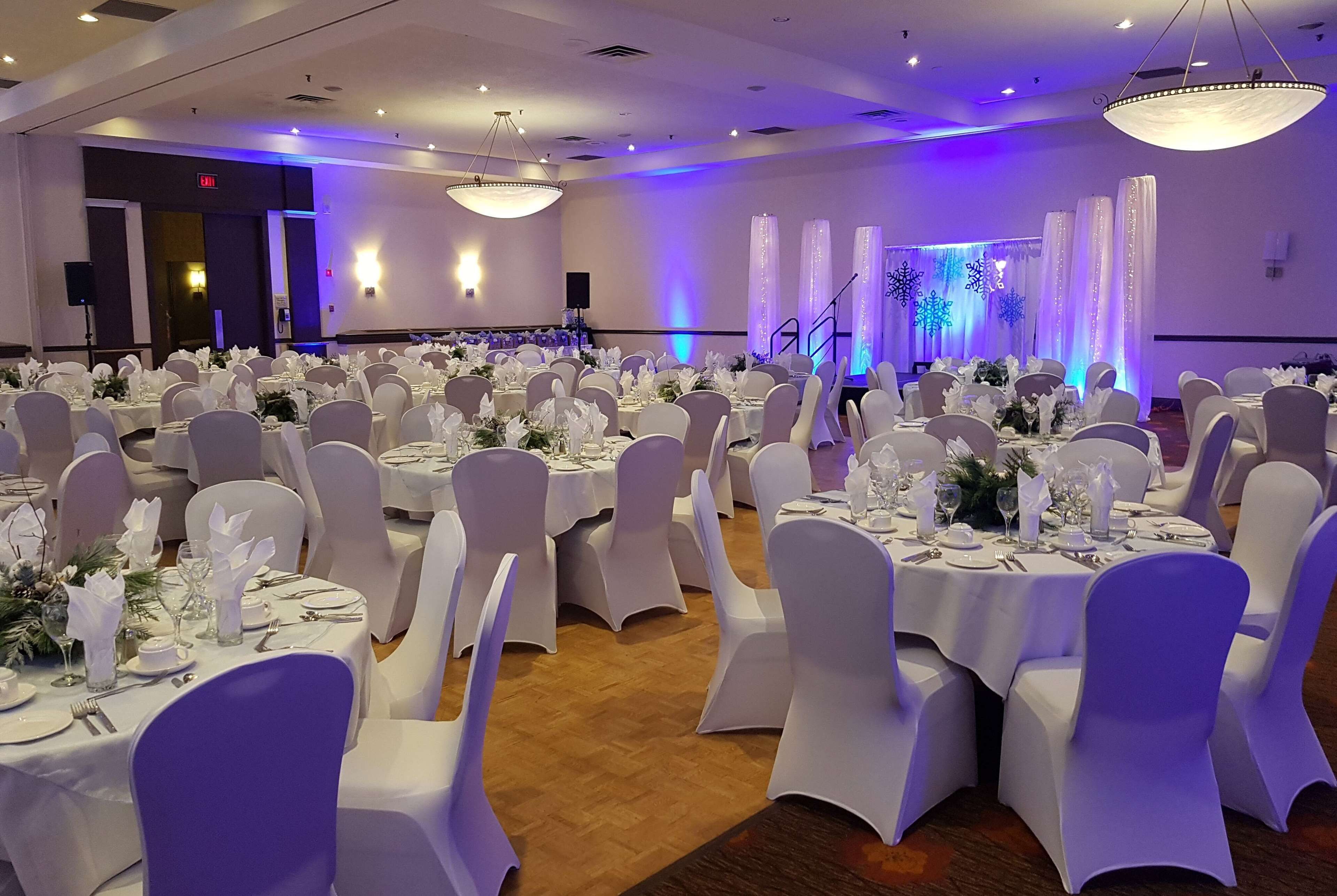 A banquet hall with round tables set for events, featuring white tablecloths and chairs.