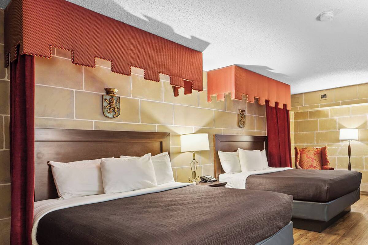 A hotel room with two beds, a stone wall, and a red curtain.