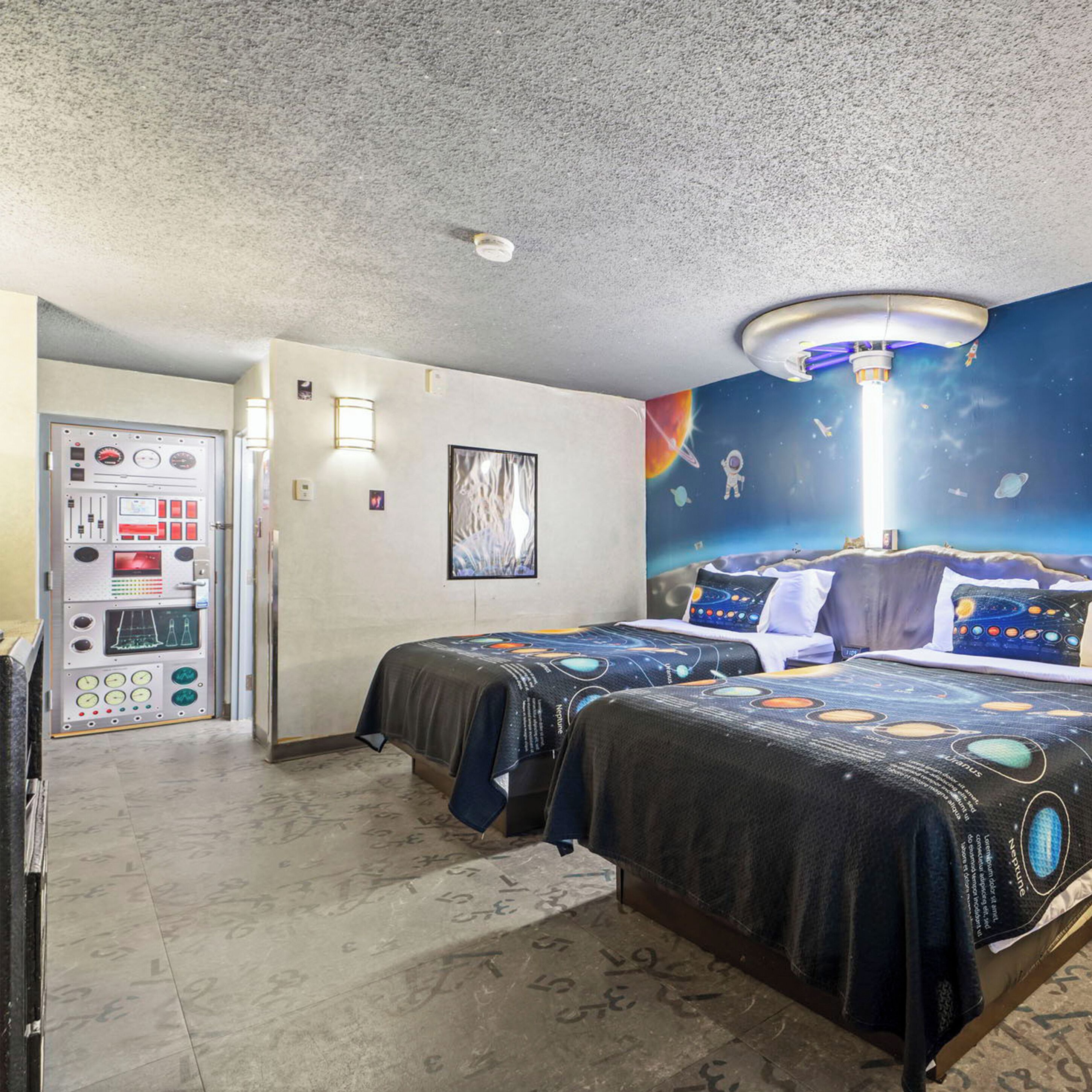 Habitación de hotel con dos camas, un panel de control, un mural espacial y una lámpara en el techo.