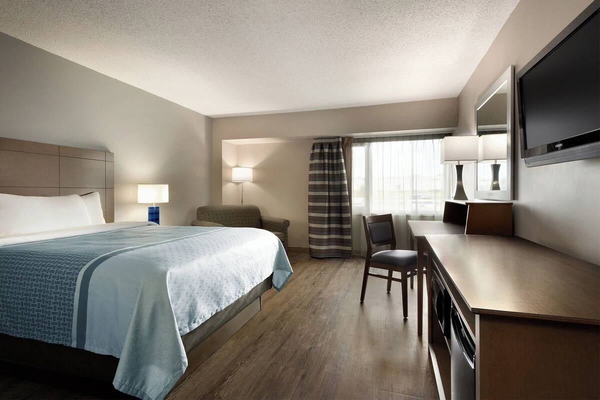 A hotel room with a bed, a desk, a chair, a TV, and a window with curtains.
