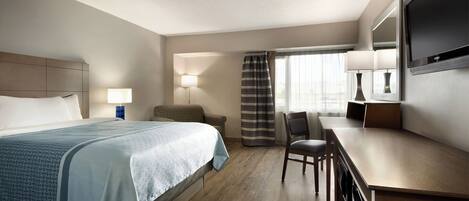 A hotel room with a bed, a desk, a chair, a TV, and a window with curtains.