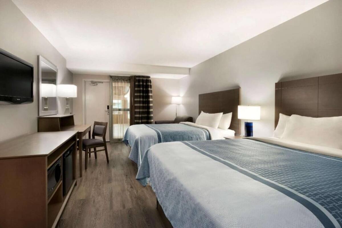 A hotel room with two beds, a desk, a chair, a TV, and a bathroom door.