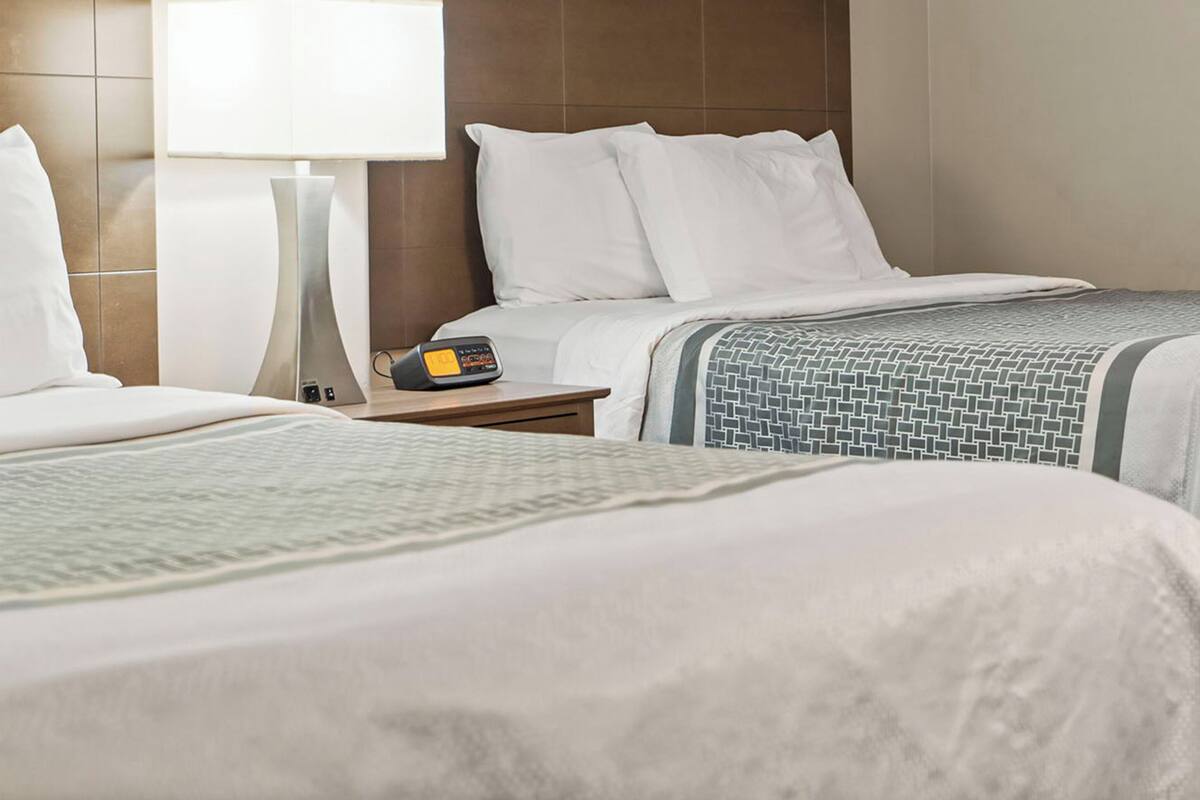 A hotel room with two beds, a nightstand, a lamp, and a digital clock.