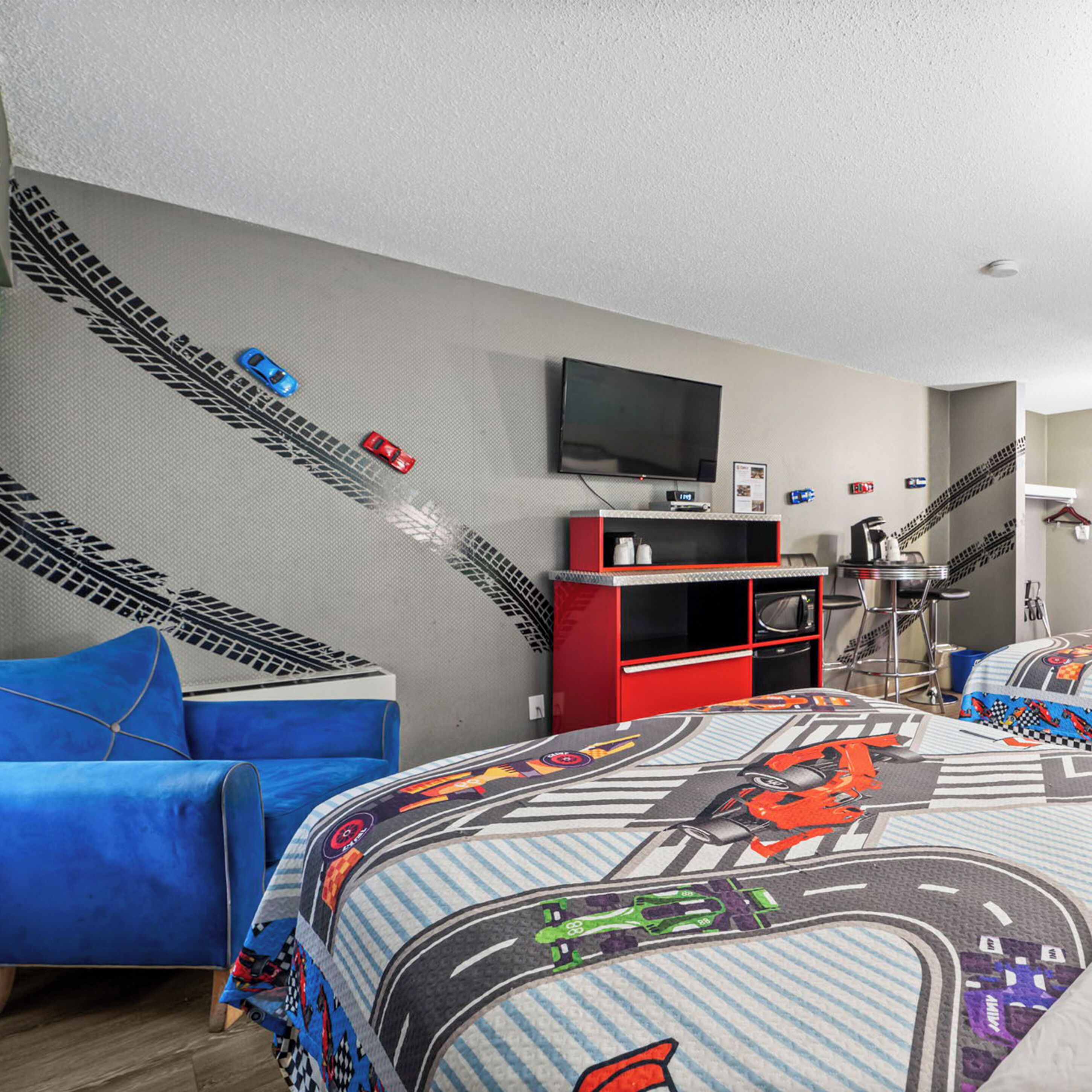 Een hotelkamer met een bed met een raceauto-design, een rode entertainmentkast, een televisie en een kleine kitchenette.