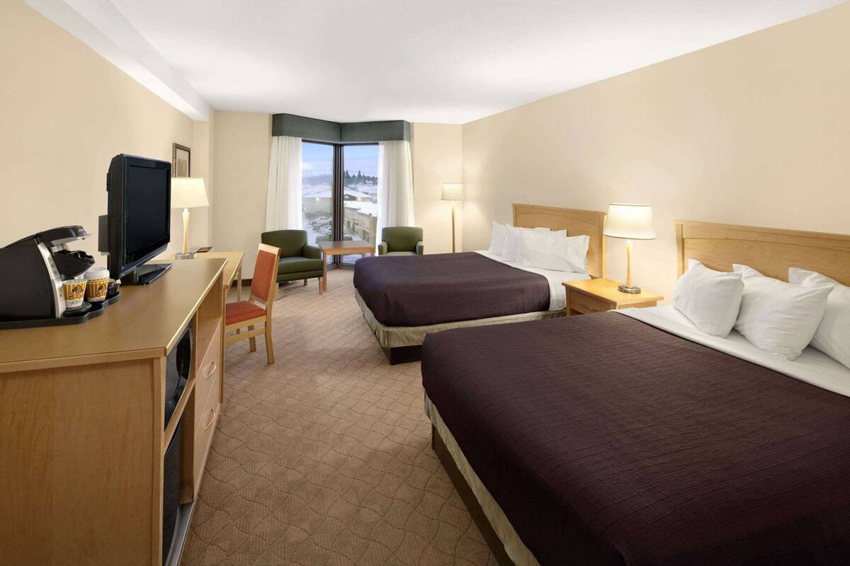 Habitación de hotel con dos camas, un escritorio con cafetera, televisión y vistas a un paisaje nevado.