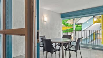 A dining area with a table and chairs, a view of a playground with a slide, and a balcony with a railing.