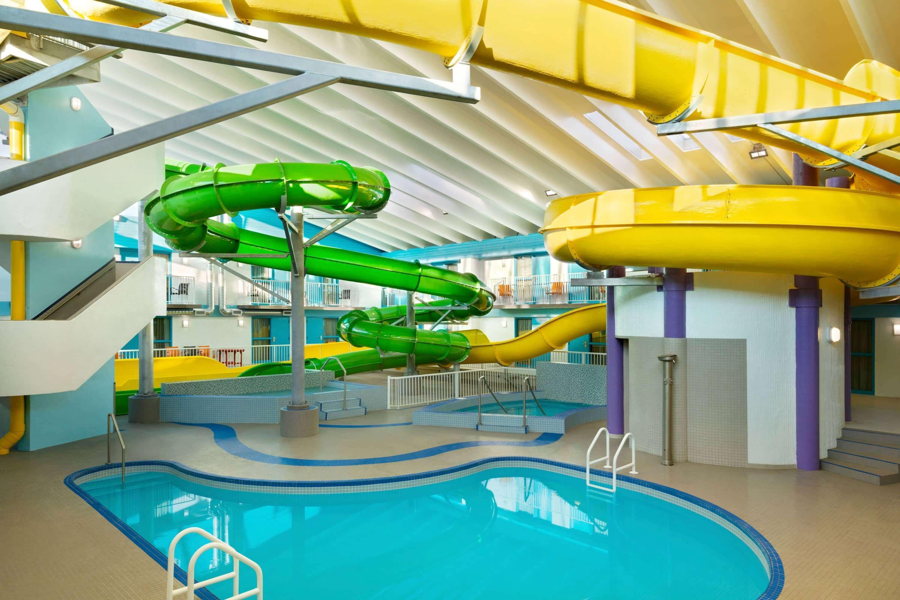 Une piscine intérieure dotée de plusieurs toboggans, d’un escalier et d’un plafond haut avec des poutres apparentes.