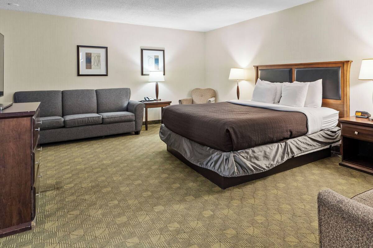 A hotel room with a bed, a sofa, a desk, and two lamps.