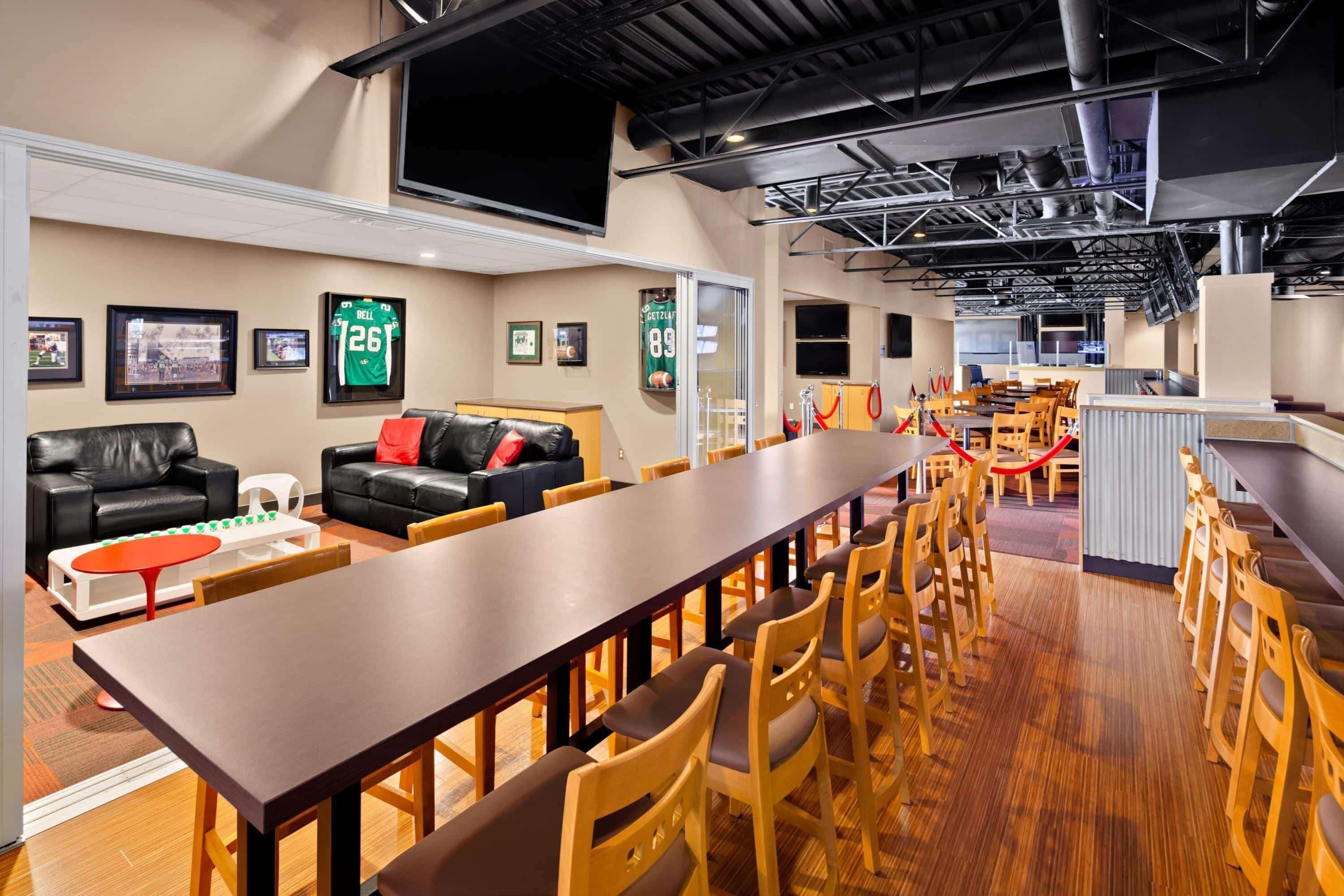 A spacious lounge area with a long wooden table, leather sofas, and wooden chairs.