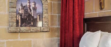 A bedroom with a stone-framed picture of a castle, red curtains, and a bed with white pillows.