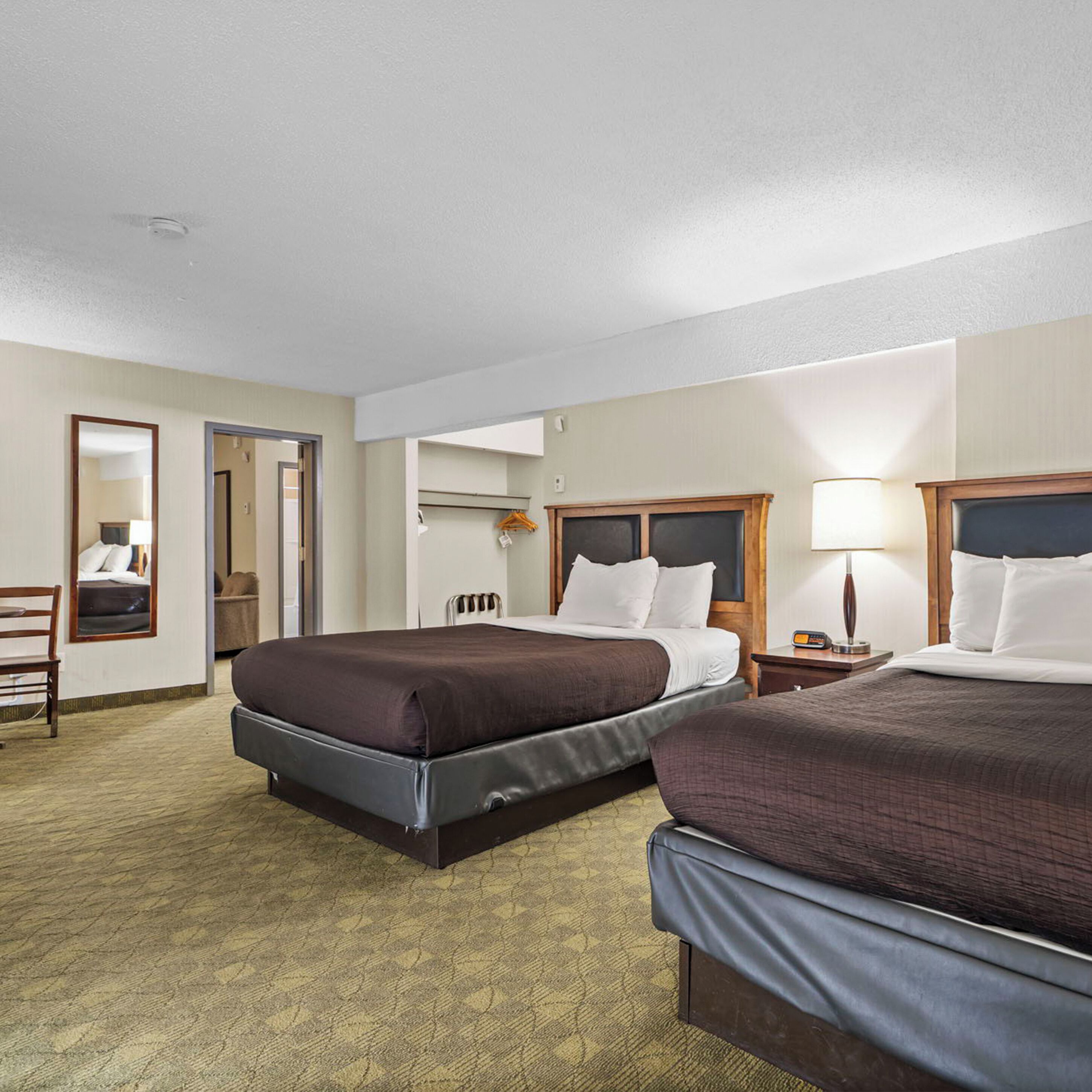 A hotel room with two beds, a chair, a desk, and a mirror.