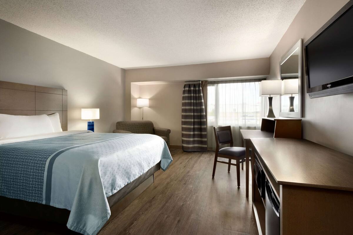 A hotel room with a bed, a desk, a chair, a TV, and a window with curtains.