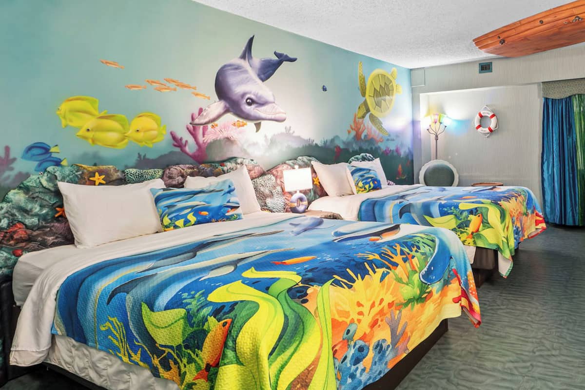 A hotel room with two beds, each with a colorful ocean-themed bedspread.