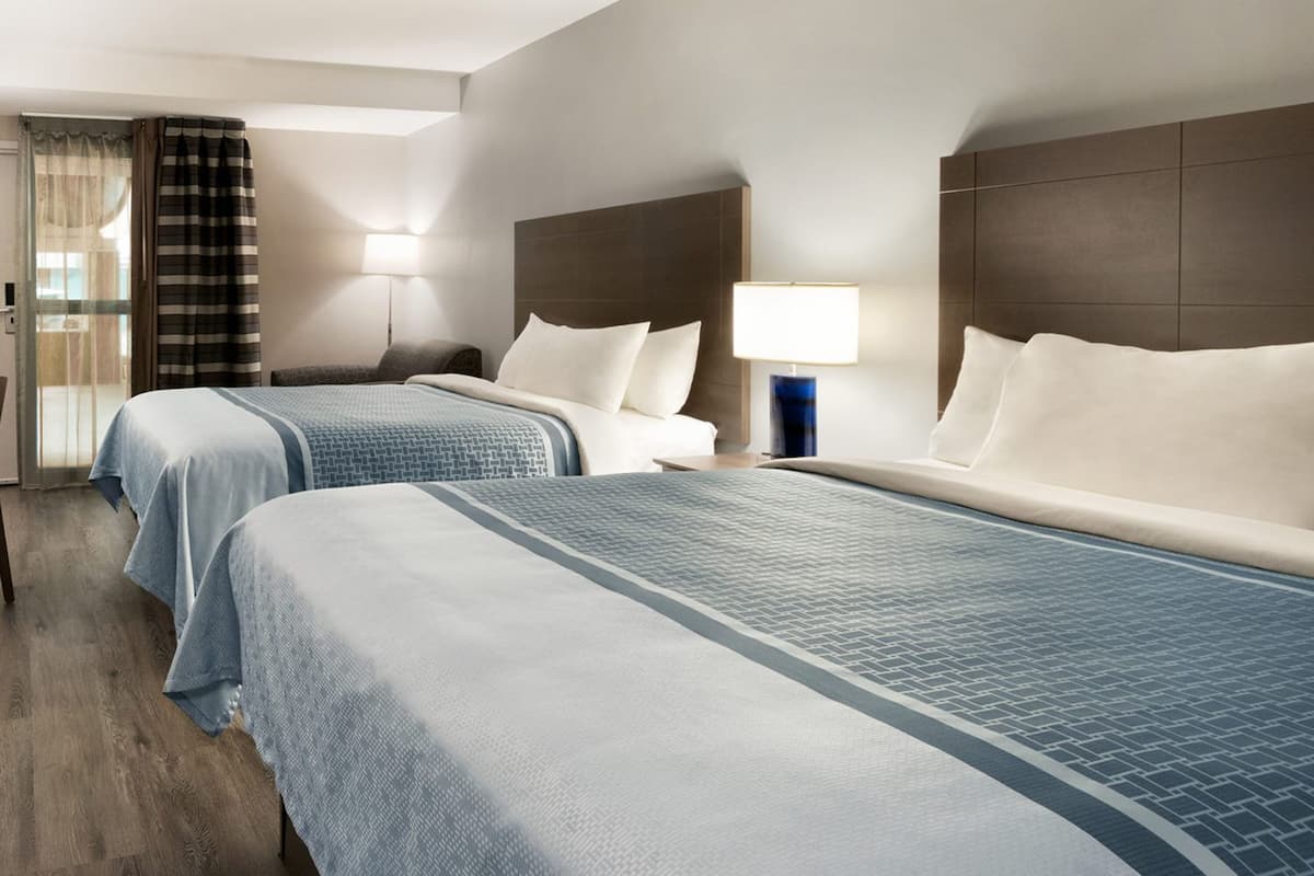 A hotel room with two beds, a headboard, a nightstand, a lamp, and a window with curtains.