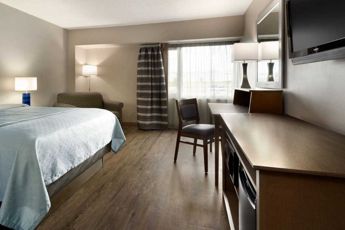 A hotel room with a bed, a desk, a chair, a TV, and a window with curtains.