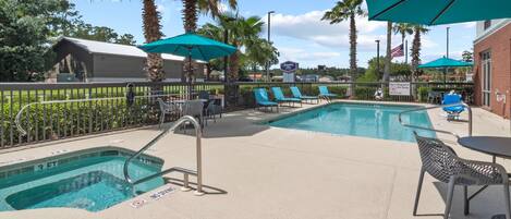 A pool area with lounge chairs, umbrellas, and a lifeguard sign.