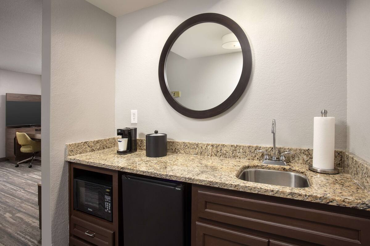 A modern kitchen with granite countertops, a built-in dishwasher, a sink, and a round mirror.