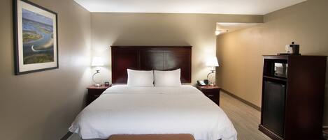 Habitación de hotel con una cama grande, dos lámparas de noche, una mesita de noche de madera, un escritorio con lámpara, un cuadro en la pared y un banco.