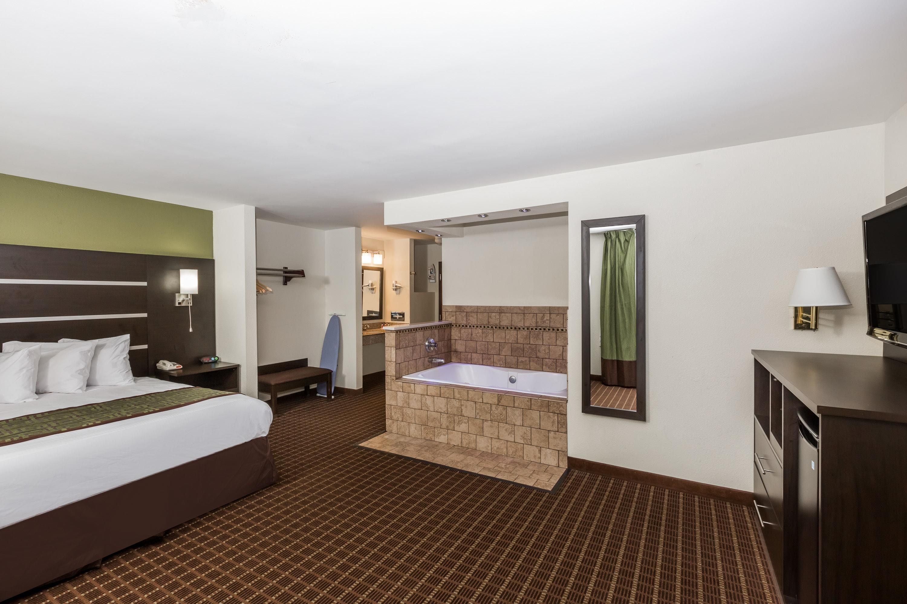 A hotel room with a bed, a bathroom with a bathtub, a mirror, and a television.